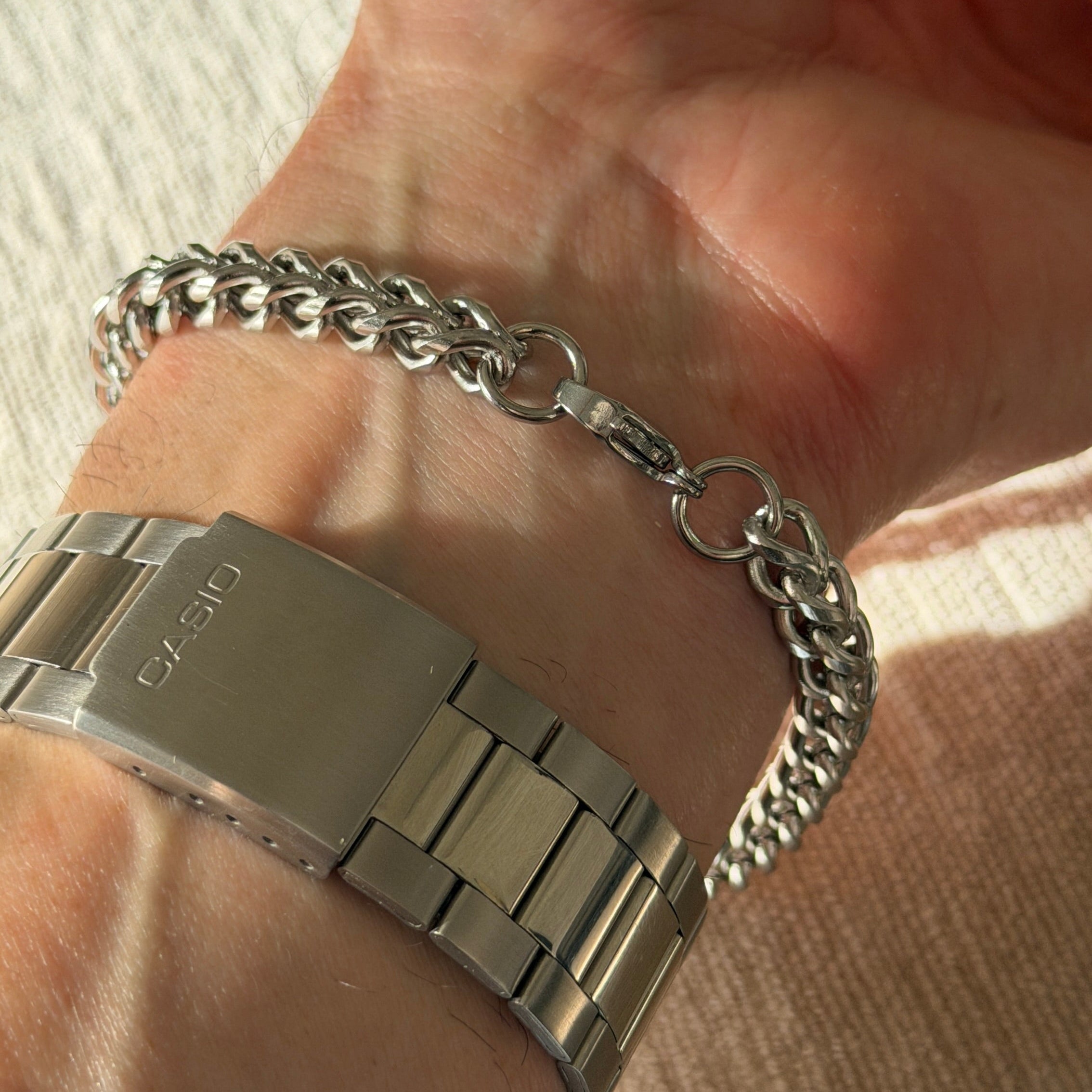 Hand wearing a silver bracelet on a neutral background