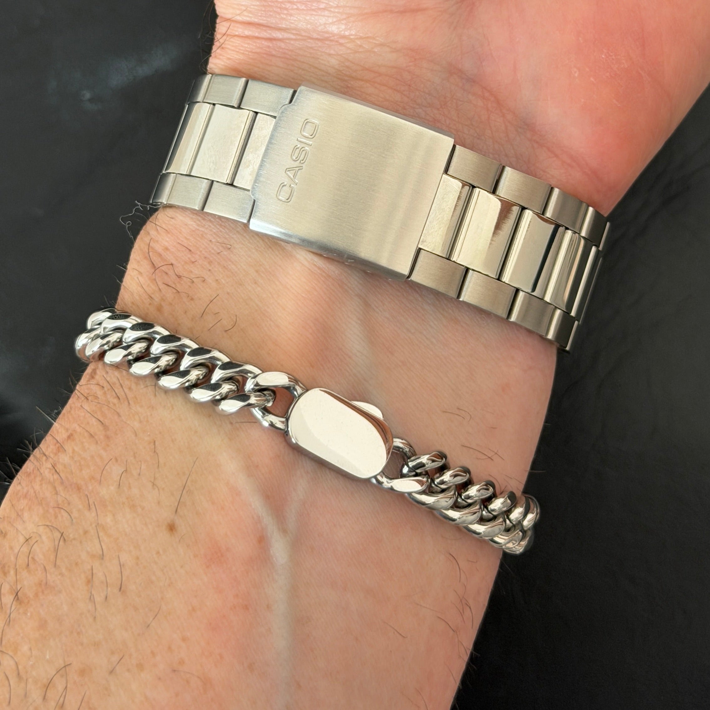 Hand wearing a silver watch and bracelet on a dark background